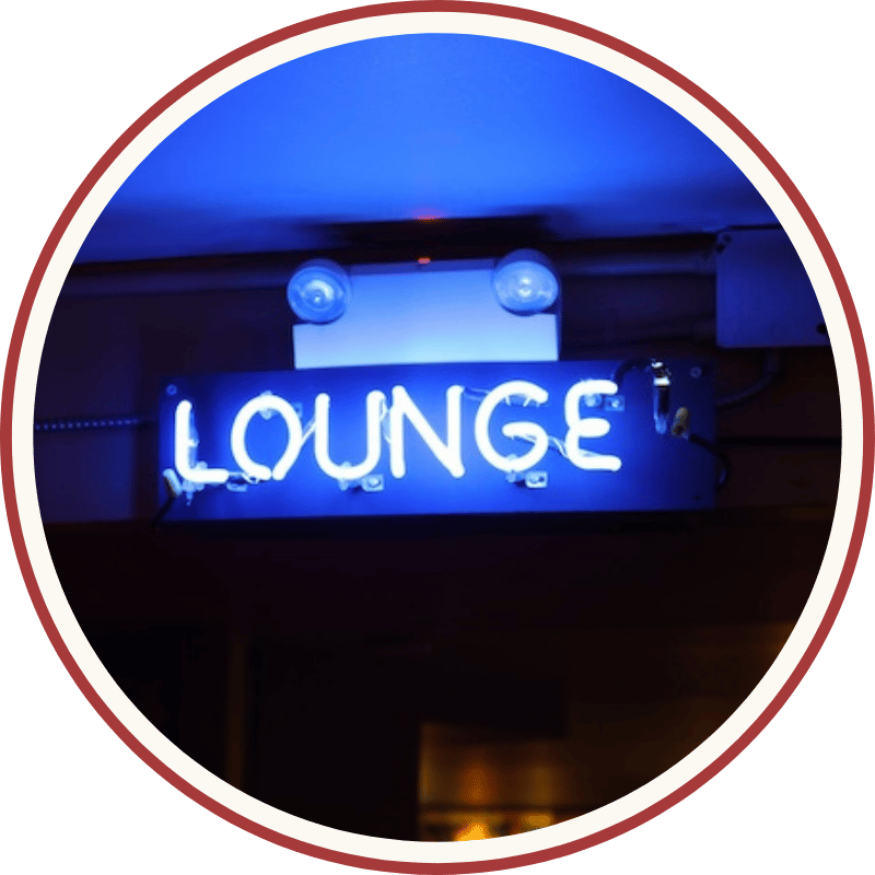 A glowing blue neon "Lounge" sign mounted on a wall, displayed in a circular frame with a red border.